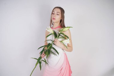 büyük gözleri ve kahverengi saçlı büyüleyici bir genç kız stüdyo beyaz bir arka planda bir moda elbise makyaj olmadan duruyor. Beyaz yemyeşil lilyum ile bir kök tutan güzel genç genç kadın.