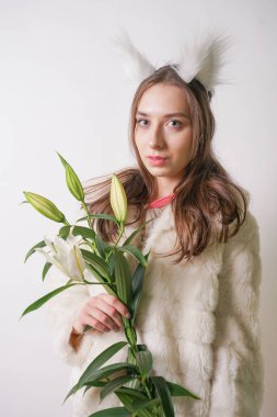 Sevimli Genç kız ayakta bir kış sıcak kürk ve kedi Tüylü kulakları kafasına, o taze lilyum bir şube tutar. Stüdyo beyaz bir arka planda bir çiçek ile kış giysileri kadın.