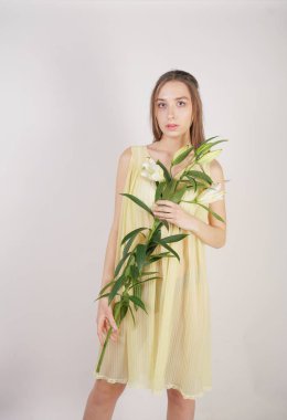 bir retro Sarı pilili şeffaf gecelik büyüleyici bir genç beyaz kız elleriyle yemyeşil bir zambak çiçek tutar ve stüdyo beyaz bir arka planda duruyor