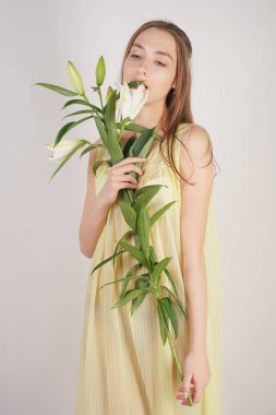 bir retro Sarı pilili şeffaf gecelik büyüleyici bir genç beyaz kız elleriyle yemyeşil bir zambak çiçek tutar ve stüdyo beyaz bir arka planda duruyor