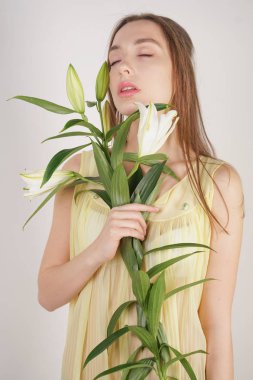 bir retro Sarı pilili şeffaf gecelik büyüleyici bir genç beyaz kız elleriyle yemyeşil bir zambak çiçek tutar ve stüdyo beyaz bir arka planda duruyor