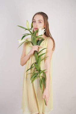 bir retro Sarı pilili şeffaf gecelik büyüleyici bir genç beyaz kız elleriyle yemyeşil bir zambak çiçek tutar ve stüdyo beyaz bir arka planda duruyor