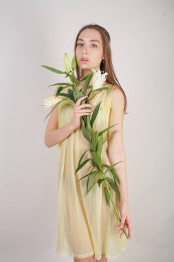 bir retro Sarı pilili şeffaf gecelik büyüleyici bir genç beyaz kız elleriyle yemyeşil bir zambak çiçek tutar ve stüdyo beyaz bir arka planda duruyor