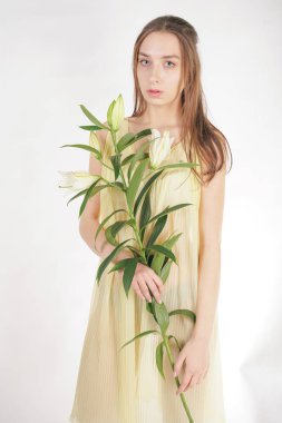 bir retro Sarı pilili şeffaf gecelik büyüleyici bir genç beyaz kız elleriyle yemyeşil bir zambak çiçek tutar ve stüdyo beyaz bir arka planda duruyor