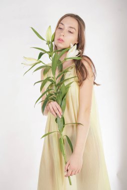 bir retro Sarı pilili şeffaf gecelik büyüleyici bir genç beyaz kız elleriyle yemyeşil bir zambak çiçek tutar ve stüdyo beyaz bir arka planda duruyor