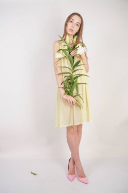 bir retro Sarı pilili şeffaf gecelik büyüleyici bir genç beyaz kız elleriyle yemyeşil bir zambak çiçek tutar ve stüdyo beyaz bir arka planda duruyor