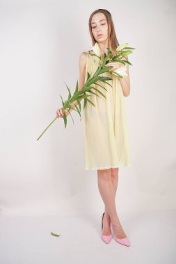 bir retro Sarı pilili şeffaf gecelik büyüleyici bir genç beyaz kız elleriyle yemyeşil bir zambak çiçek tutar ve stüdyo beyaz bir arka planda duruyor