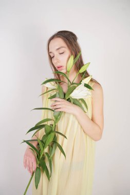 bir retro Sarı pilili şeffaf gecelik büyüleyici bir genç beyaz kız elleriyle yemyeşil bir zambak çiçek tutar ve stüdyo beyaz bir arka planda duruyor