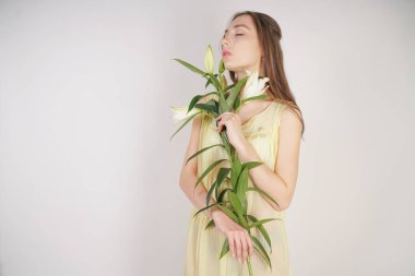 bir retro Sarı pilili şeffaf gecelik büyüleyici bir genç beyaz kız elleriyle yemyeşil bir zambak çiçek tutar ve stüdyo beyaz bir arka planda duruyor