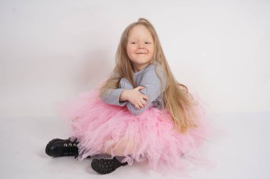 uzun sarışın saçlı küçük beyaz kız Gri tişört ve beyaz stüdyo arka planda pembe kabarık etek oturan tek başına