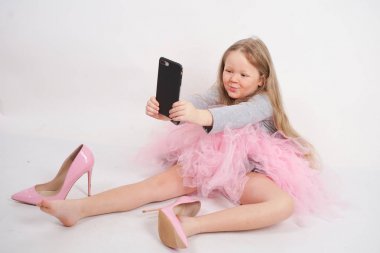 biraz beyaz çocuk kız oturur ve anne yüksek topuklu pembe ayakkabı koyar, beyaz stüdyo arka plan üzerinde onun akıllı telefonda tüm resimleri ve selfie 'ler alarak