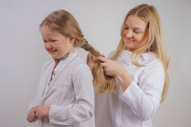 Anne ve kızı beyaz gömlek uzun sarışın saç stüdyo katı bir arka planda poz ile. büyüleyici bir aile birbirleriyle ilgilenir ve örgü yapar.