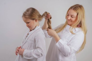 Anne ve kızı beyaz gömlek uzun sarışın saç stüdyo katı bir arka planda poz ile. büyüleyici bir aile birbirleriyle ilgilenir ve örgü yapar.