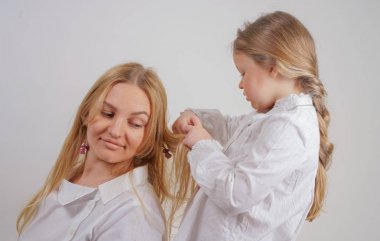 Anne ve kızı beyaz gömlek uzun sarışın saç stüdyo katı bir arka planda poz ile. büyüleyici bir aile birbirleriyle ilgilenir ve örgü yapar.