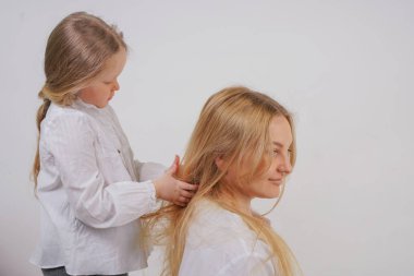 Anne ve kızı beyaz gömlek uzun sarışın saç stüdyo katı bir arka planda poz ile. büyüleyici bir aile birbirleriyle ilgilenir ve örgü yapar.