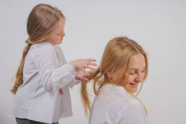 Anne ve kızı beyaz gömlek uzun sarışın saç stüdyo katı bir arka planda poz ile. büyüleyici bir aile birbirleriyle ilgilenir ve örgü yapar.