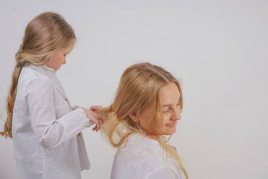 Anne ve kızı beyaz gömlek uzun sarışın saç stüdyo katı bir arka planda poz ile. büyüleyici bir aile birbirleriyle ilgilenir ve örgü yapar.