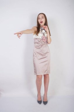 beautiful caucasian teen girl stands in a short evening dress and mocks the interlocutor, humiliating, on a white background in the Studio clipart