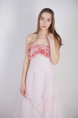 büyüleyici bir genç beyaz kız göğsünde çiçek yaprakları ile pembe uzun balo elbisesi duruyor ve stüdyo beyaz bir arka planda pozlar