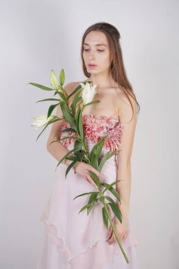 güzel bir elbise sevimli genç beyaz kız elinde gür zambak çiçek tutar ve tek başına stüdyo beyaz bir arka planda duruyor