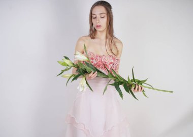 güzel bir elbise sevimli genç beyaz kız elinde gür zambak çiçek tutar ve tek başına stüdyo beyaz bir arka planda duruyor