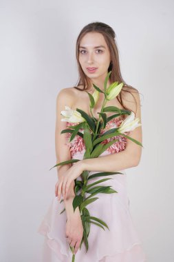 güzel bir elbise sevimli genç beyaz kız elinde gür zambak çiçek tutar ve tek başına stüdyo beyaz bir arka planda duruyor