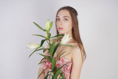 güzel bir elbise sevimli genç beyaz kız elinde gür zambak çiçek tutar ve tek başına stüdyo beyaz bir arka planda duruyor