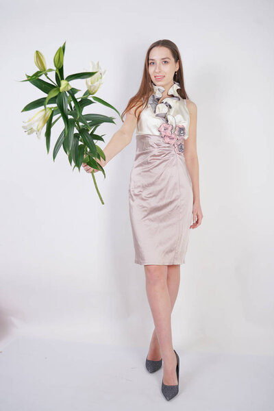 charming young caucasian girl in a pretty dress holds a lush Lily flower in her hands and stands on a white background in the Studio alone