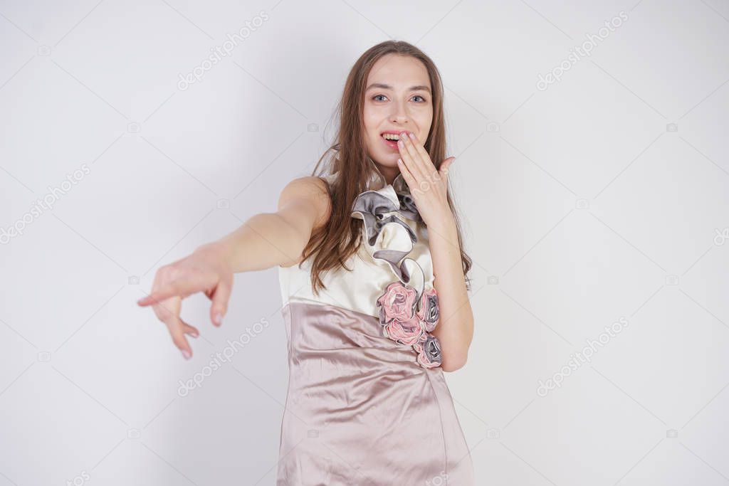beautiful caucasian teen girl stands in a short evening dress and mocks the interlocutor, humiliating, on a white background in the Studio