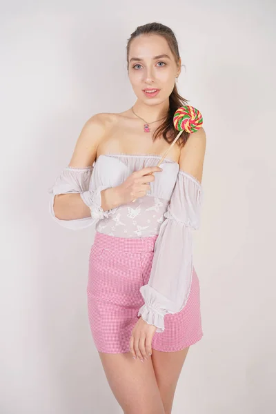 可爱的女性高加索女孩站在一个透明薄的夏季衬衫与一个圆的五颜六色的糖果在她的手在一个白色的背景在演播室 — 图库照片