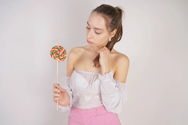 a cute thin caucasian girl in a white summer clothes looks at a delicious candy, thinks whether it is worth eating it, and does not wanna to get fat