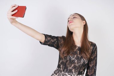 sevimli Kafkas dostu kız elinde bir cep telefonu ile standları ve tek başına stüdyo beyaz bir arka planda mutlu bir duygusal selfie alır