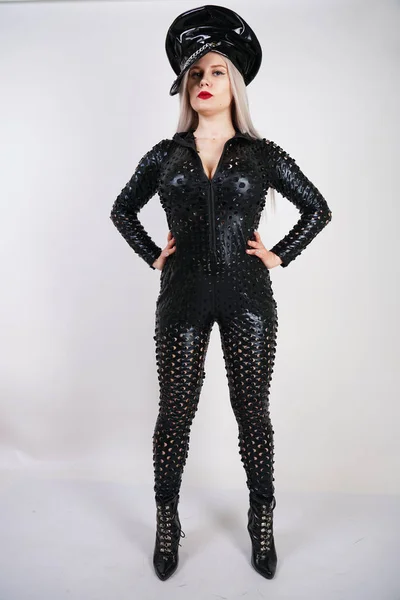 cruel fashionable bdsm lady with curves dressed in black catsuit with sexy holes and posing on a white background in the Studio