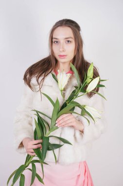 Stüdyo arka planda lilyum bir şube ile beyaz bir kürk ceket kadınsı kız