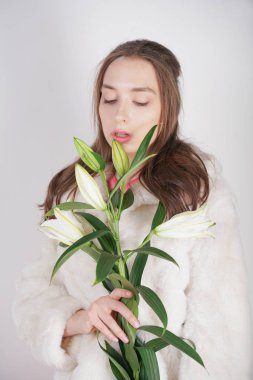 Stüdyo arka planda lilyum bir şube ile beyaz bir kürk ceket kadınsı kız