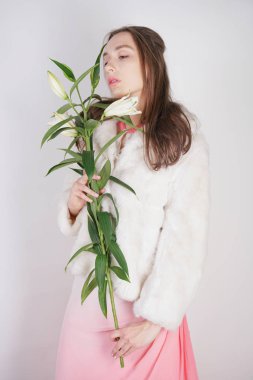 Stüdyo arka planda lilyum bir şube ile beyaz bir kürk ceket kadınsı kız