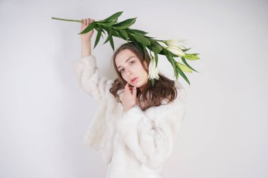 Stüdyo arka planda lilyum bir şube ile beyaz bir kürk ceket kadınsı kız