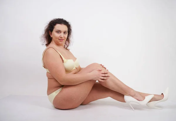 feminine woman with plus size body in yellow lingerie posing on white background in Studio