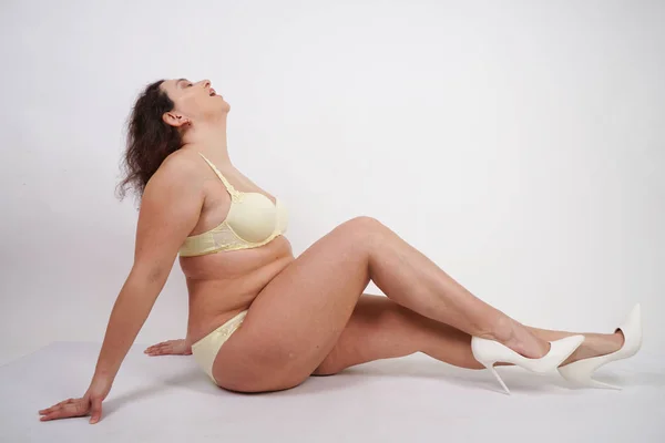 feminine woman with plus size body in yellow lingerie posing on white background in Studio