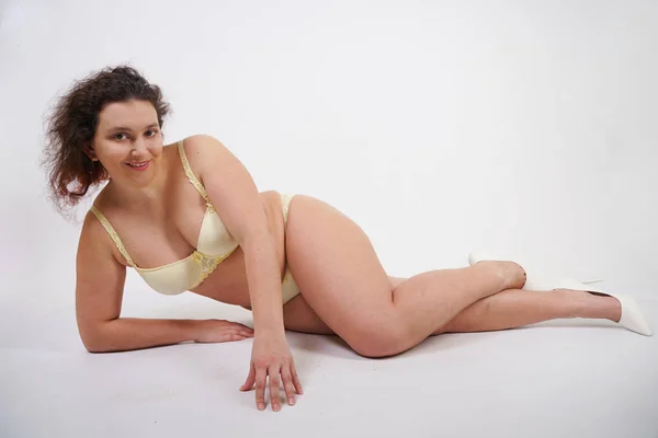 feminine woman with plus size body in yellow lingerie posing on white background in Studio