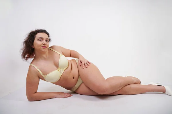 feminine woman with plus size body in yellow lingerie posing on white background in Studio