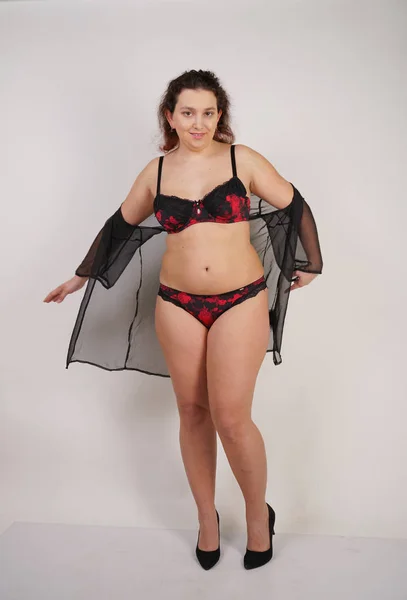 feminine chubby woman with plus size body in black lingerie posing on white background in Studio