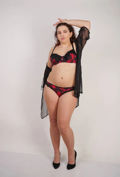 feminine chubby woman with plus size body in black lingerie posing on white background in Studio