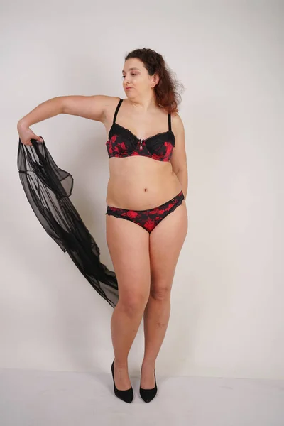 feminine chubby woman with plus size body in black lingerie posing on white background in Studio