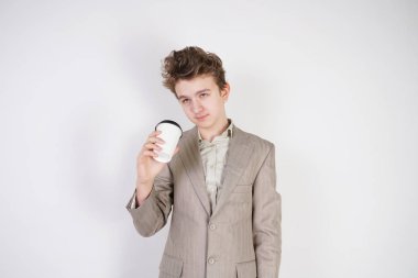 beyaz stüdyo arka plan üzerinde elinde kahve kağıt Fincan ile gri iş elbisesi içinde yorgun genç çocuk