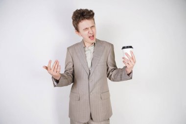 beyaz stüdyo arka plan üzerinde elinde kahve kağıt Fincan ile gri iş elbisesi içinde yorgun genç çocuk