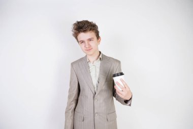 beyaz stüdyo arka plan üzerinde elinde kahve kağıt Fincan ile gri iş elbisesi içinde yorgun genç çocuk