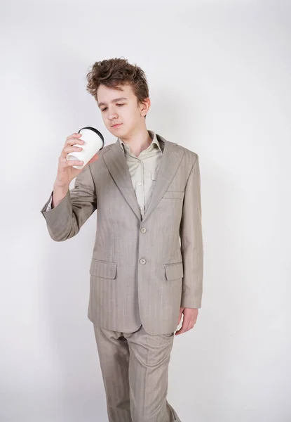 疲惫的青少年男孩在灰色西装与纸杯咖啡在白色工作室背景 — 图库照片
