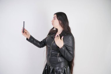 kaya tarzı siyah deri ceket büyüleyici esmer Studio beyaz bir arka plan üzerinde bir akıllı telefon ile duruyor