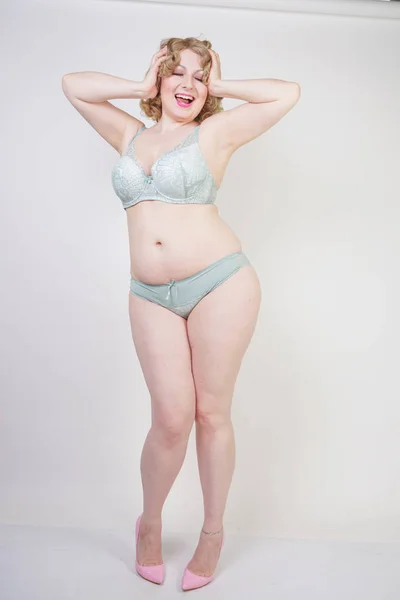 Pretty caucasian chubby woman with plus size body and pale skin wearing green lace sexy underwear on white studio background